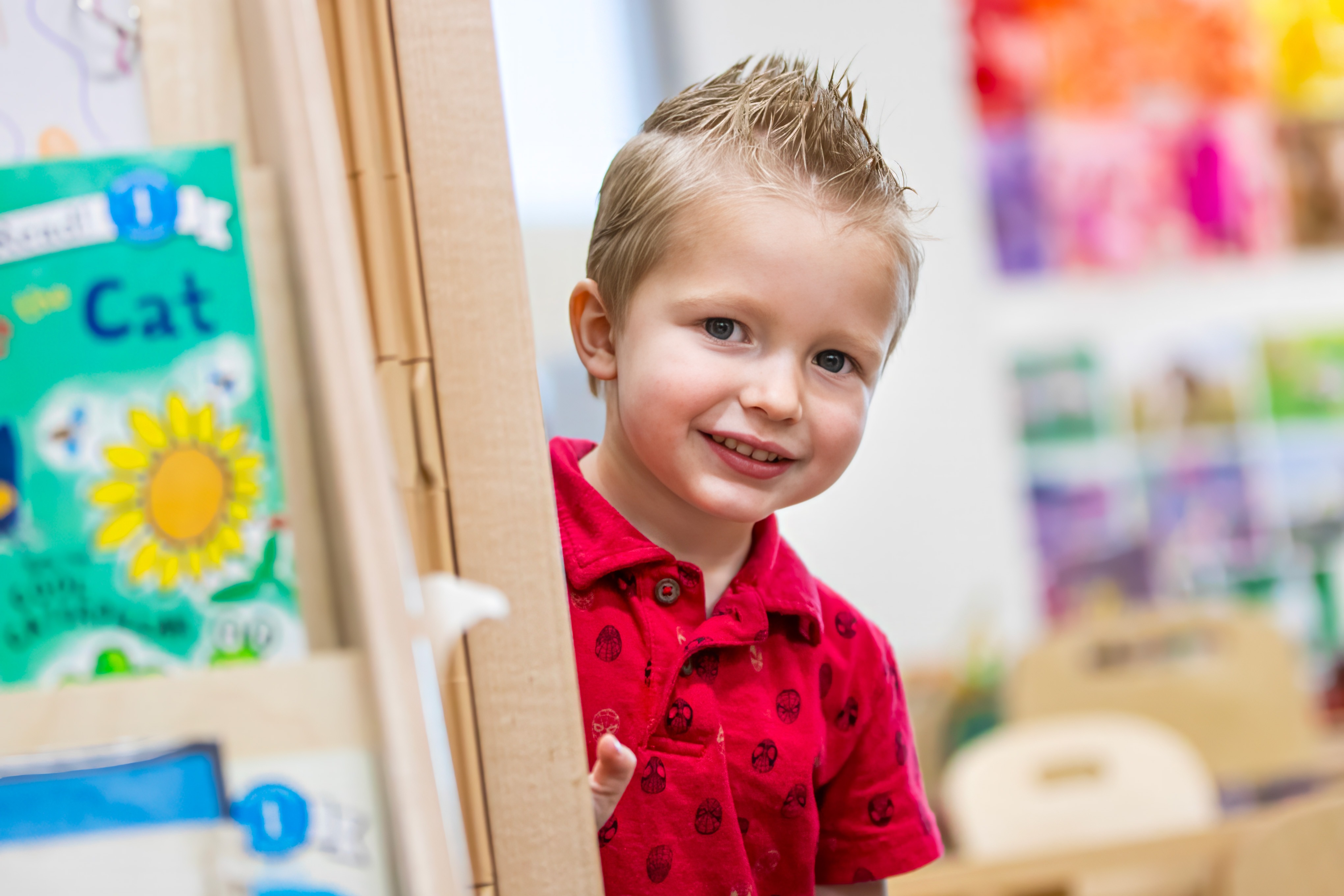 A young boy peeks our from behind a bookshelf.