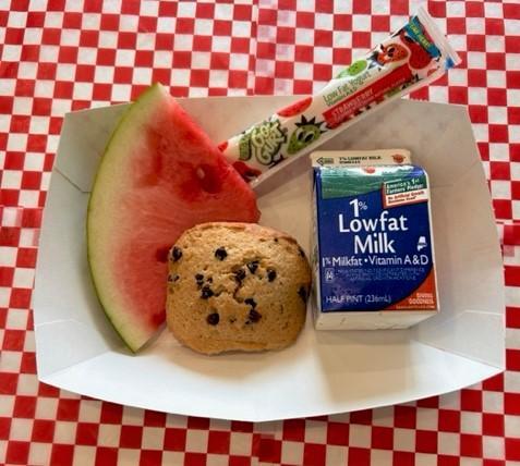 A watermelon slice, cookie, and milk on a plate