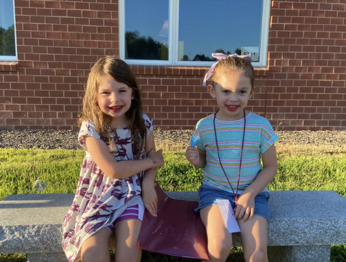 Two young girls sitting on a bench outside, enjoying each other's company and the pleasant weather.