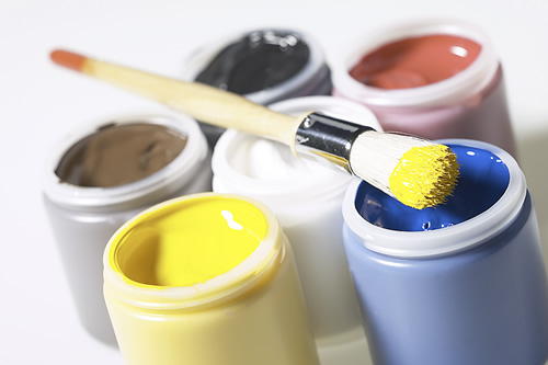 Assorted paint brushes and colorful paint in jars on a table.
