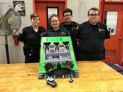 Police officers posing with a model police station, showcasing their dedication to law enforcement.