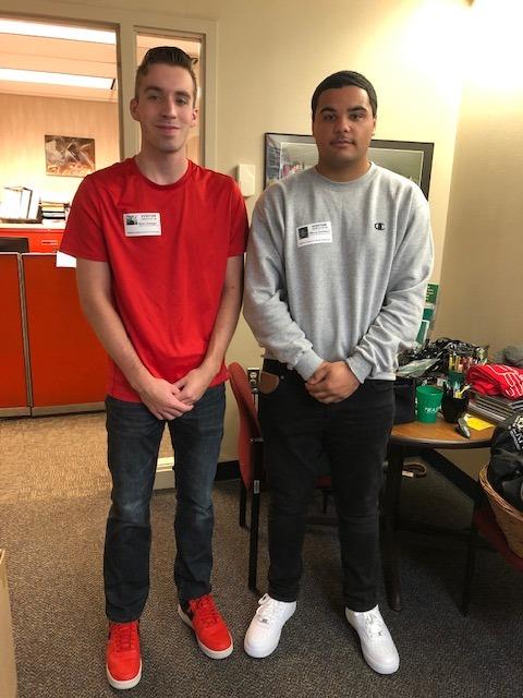 Two young men in red shirts and black shoes standing next to each other, smiling and posing for a photo.