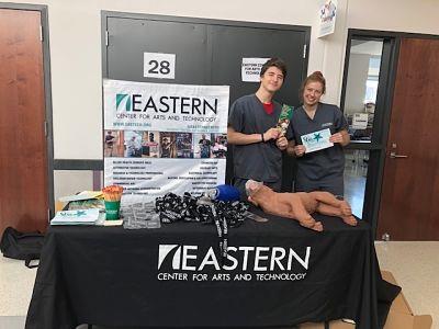 Two individuals positioned behind a table displaying an "Eastern" sign.