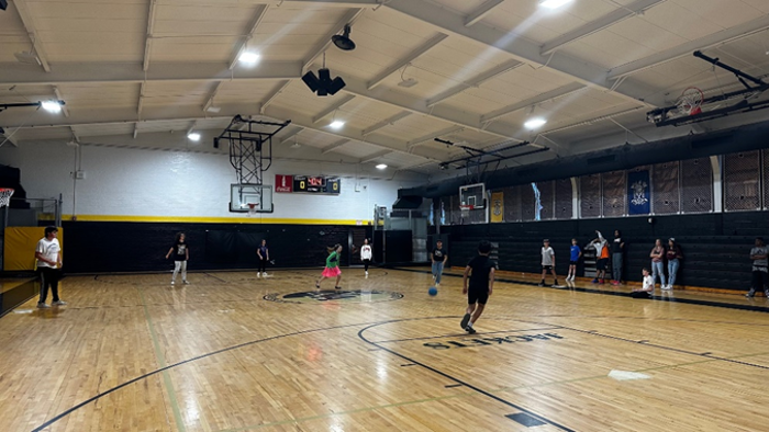 A gymnasium with middle-school aged students playing basketball. The gym has coverings over the windows. 