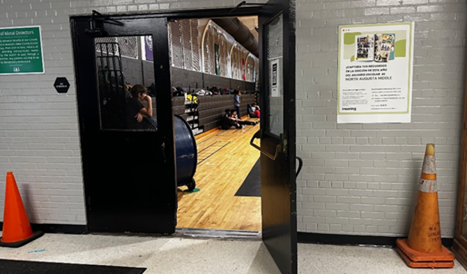 Black Door proped open to a gym. Orange cones flank the doors to an open space painted gray. 