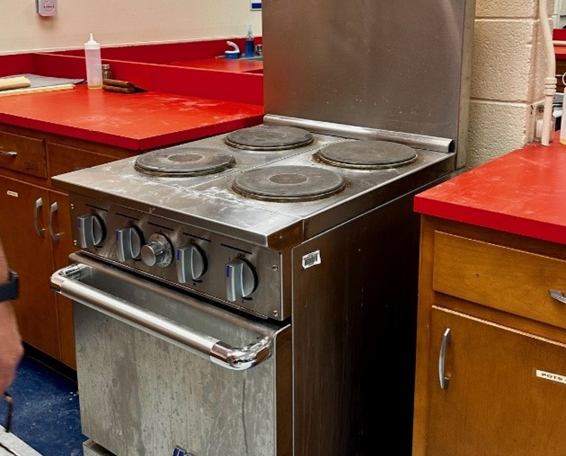 An old stove next to a wooden cabinet with red countertops. 