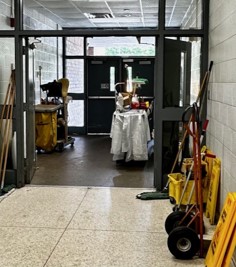 Yellow caution signs, a custodial cart, mops, and general clearning equipment in a doorway. 