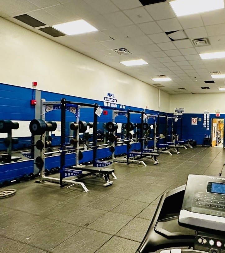 Athletic weight room with multiple sets of barbells. The walls are white with blue stripes. 