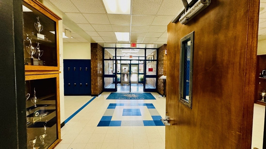 Entrance area with trophy cases to the left and dark blue lockers, a wall of windows in front. 