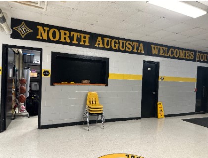 A cinder block space that resembles a ticket booth in an athletic gym with a yellow chair. 