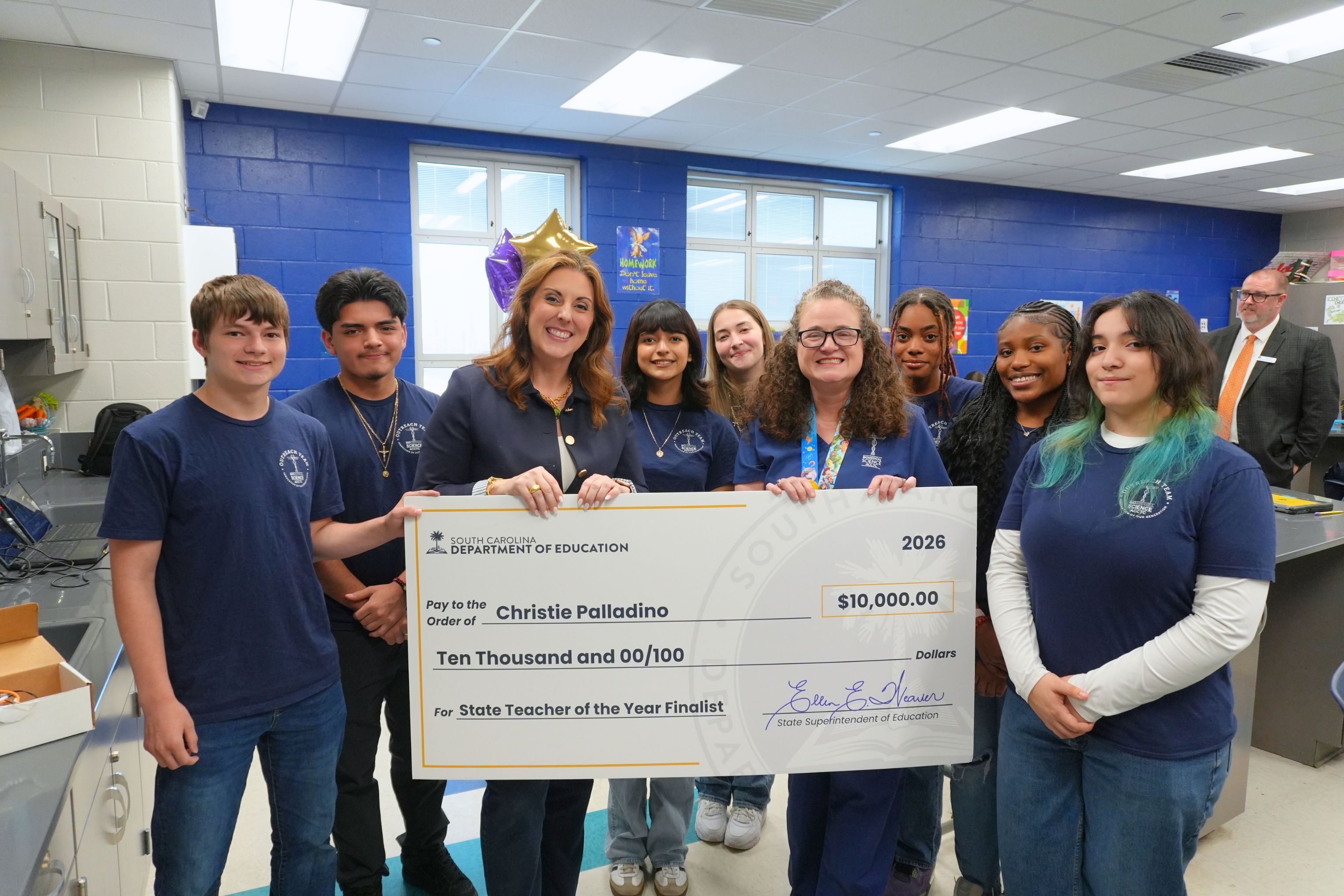 Dr. Palladino smiling with large check and students.