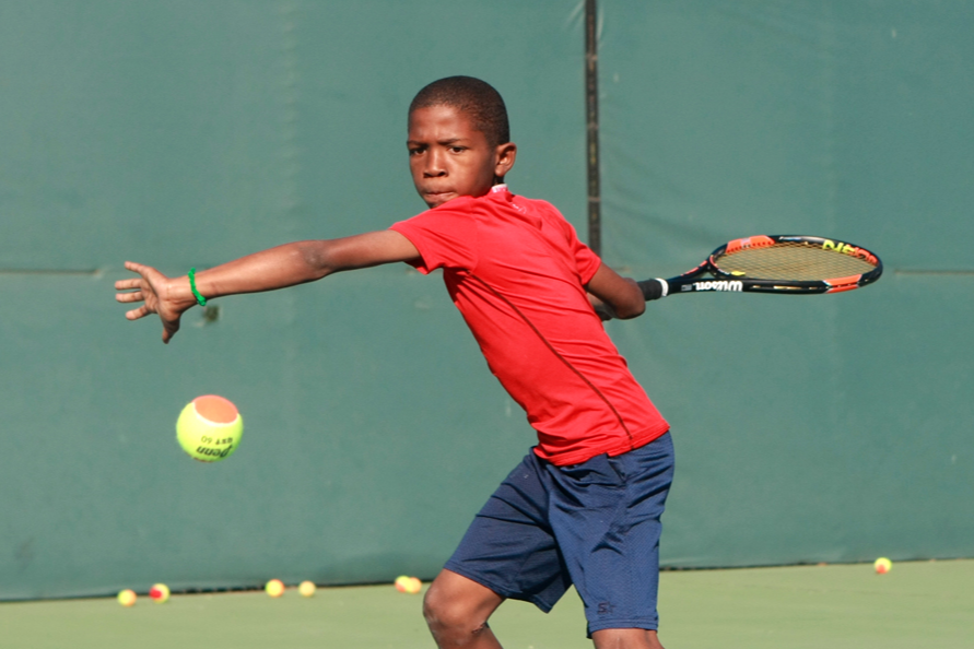 Young kid swinging tennis racquet at a tennis ball