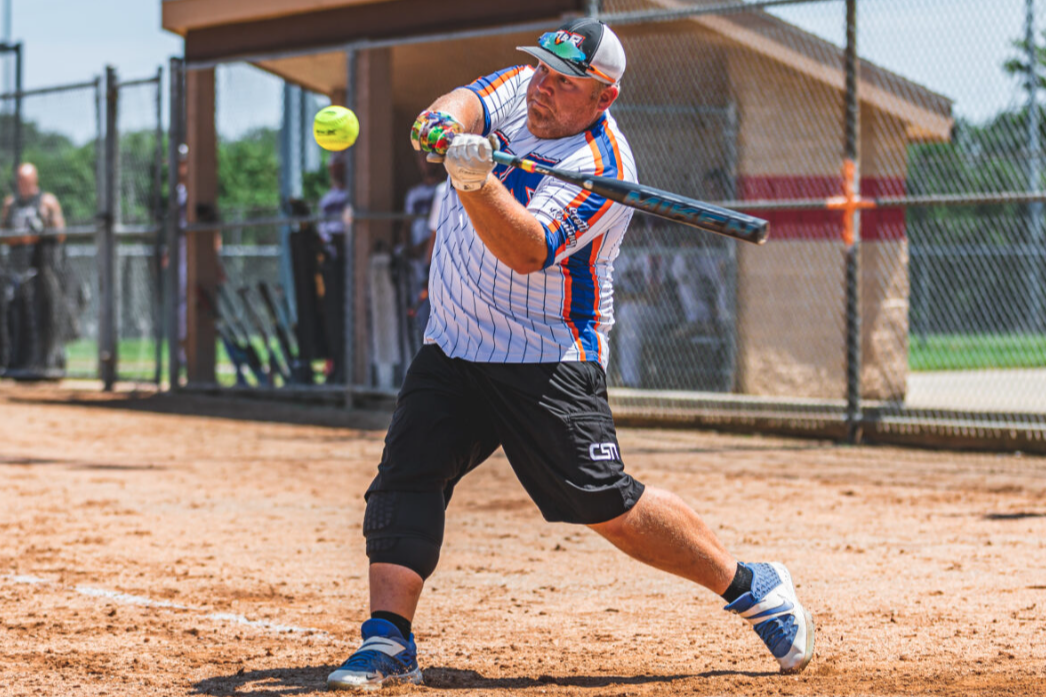 Guy hitting a softball with a bat