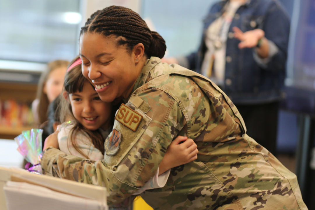 Mom and daughter embrace. Mom is in military fatigues and is visiting and supporting her daughter at a school hosted event.