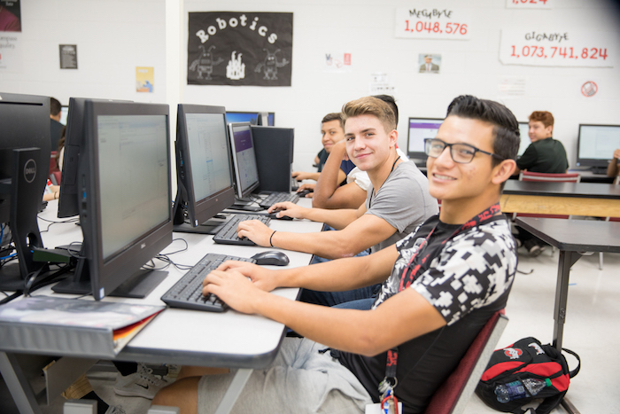 Students smiling in front of computers