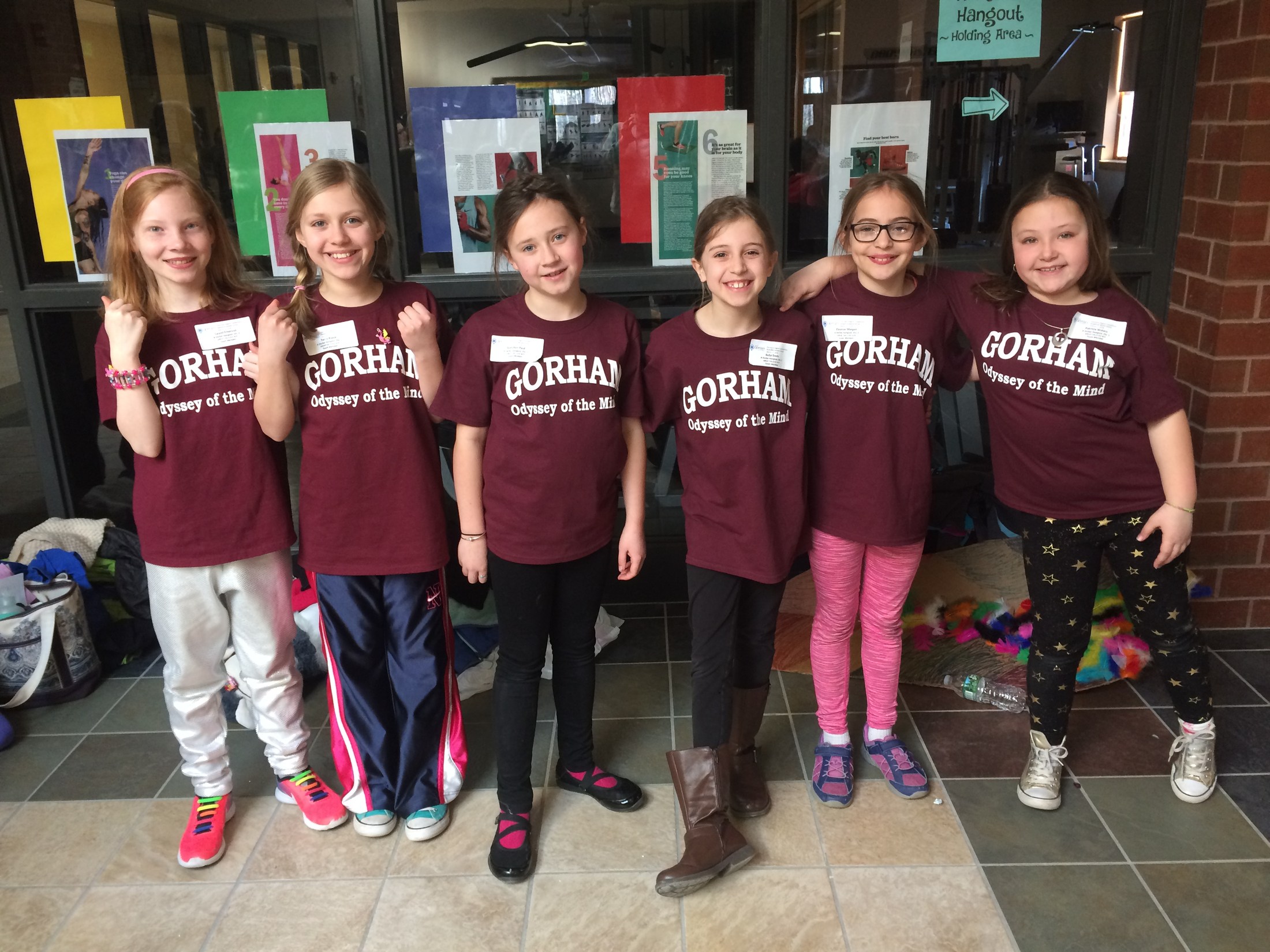 Group of six girls wearing maroon shirts standing by a door.