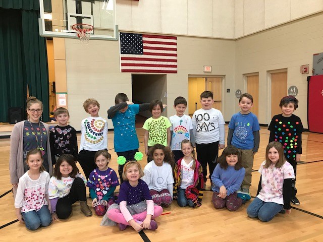 A group of children smiling and posing for a picture in a gymnasium, capturing a joyful moment of togetherness.