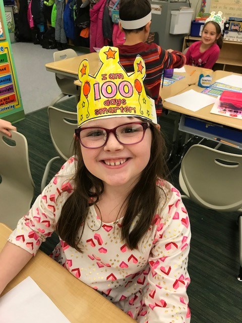 A young girl with a crown and glasses sitting at a table.