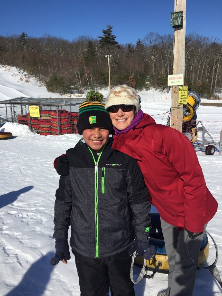 A man and a woman standing in the snow, holding hands and smiling, surrounded by a winter wonderland.