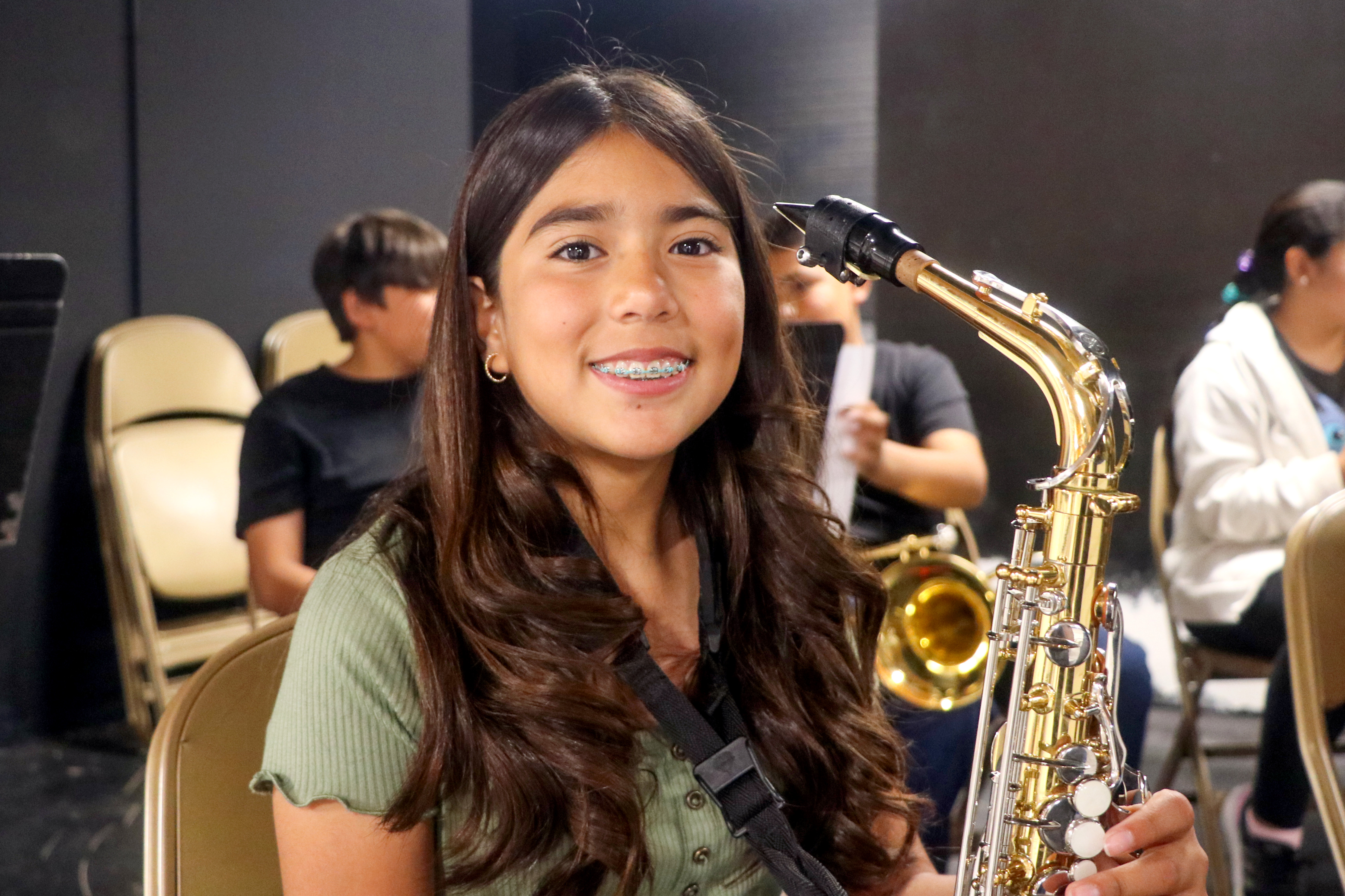 A young girl smiles while holding a saxophone. holding her 