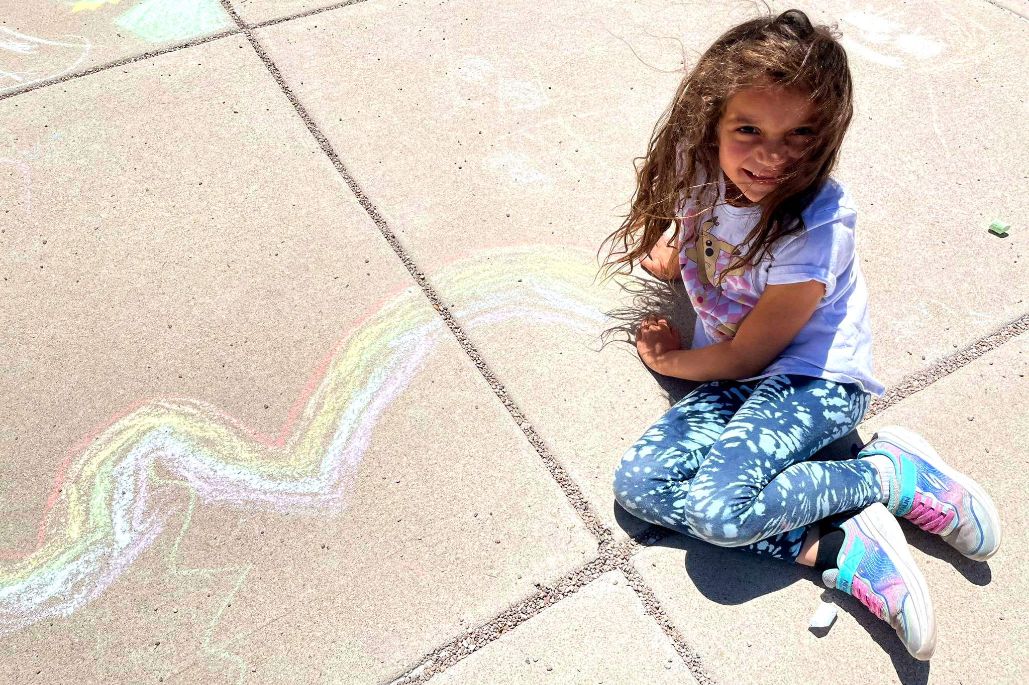 Girl sitting next to her chalk art creation.
