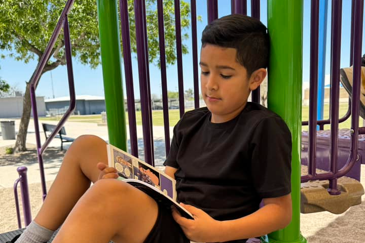 A young boy reads a book on the playground equipment.