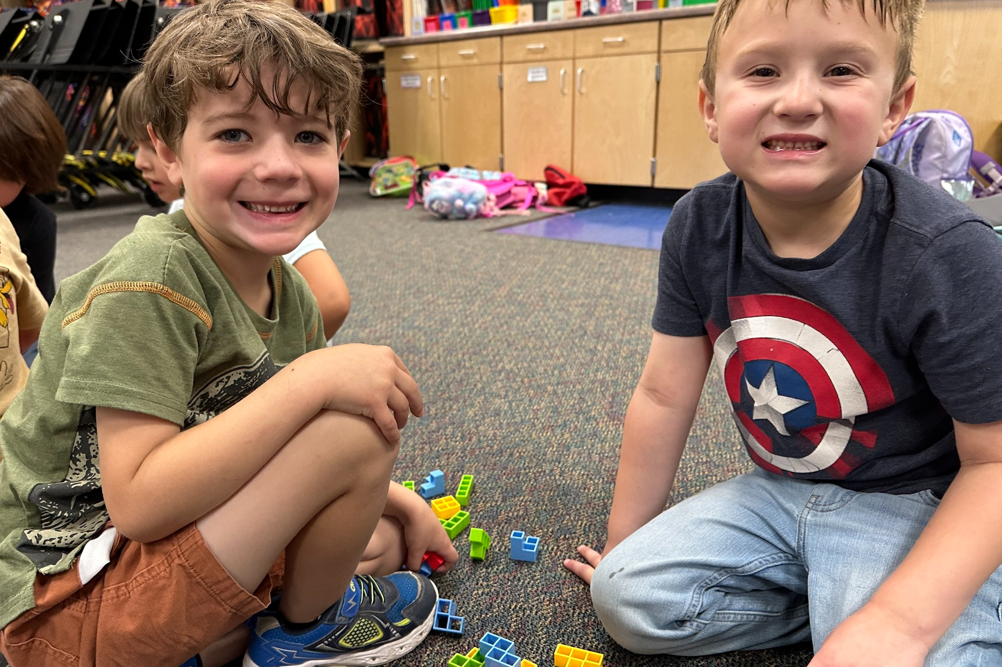Two boys smile at the camera, with Legos scattered nearby.