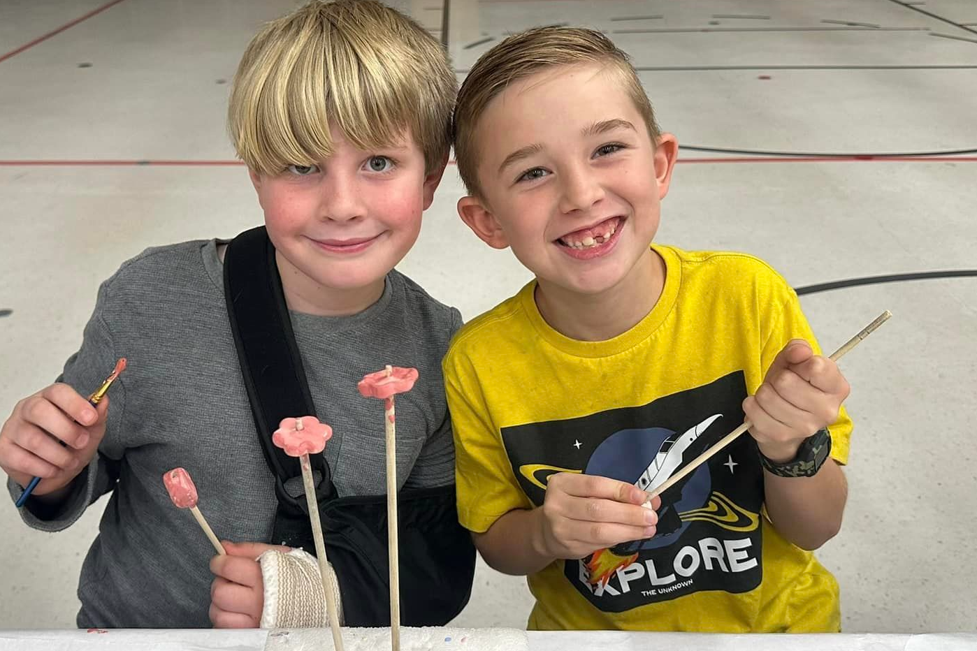 Two young boys smile while holding paintbrushes.