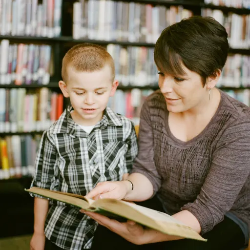 A woman reading a book to a boy in a library