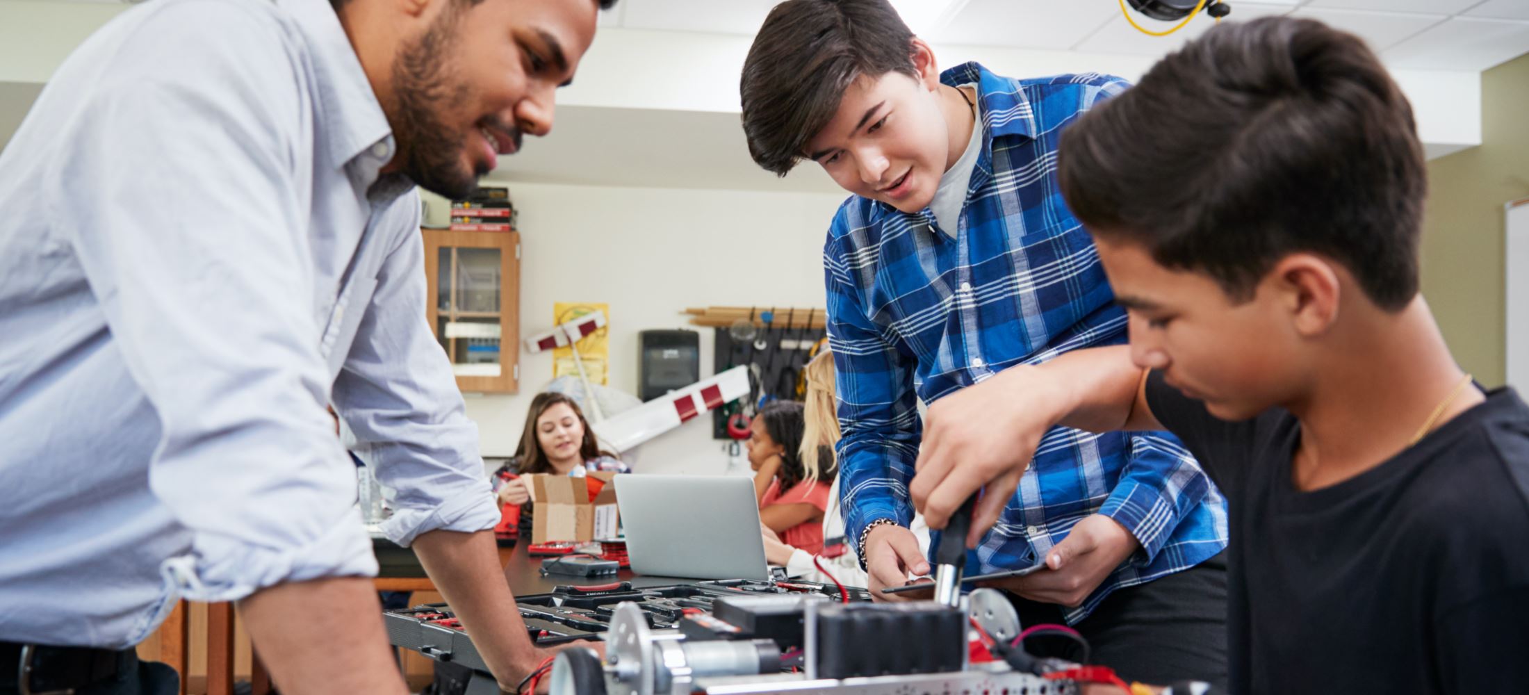 teacher, student and younger student working on robotics at a table