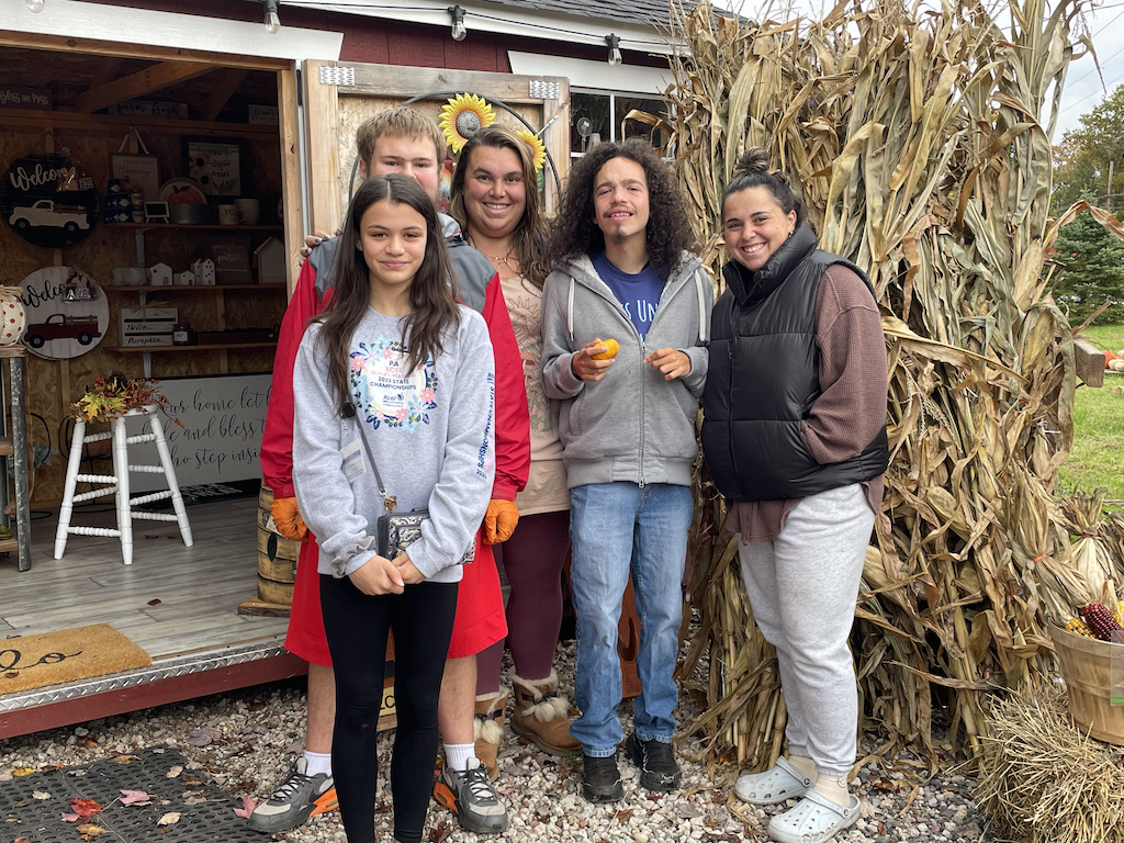 Students pose in front of cornstalks with pumpkin