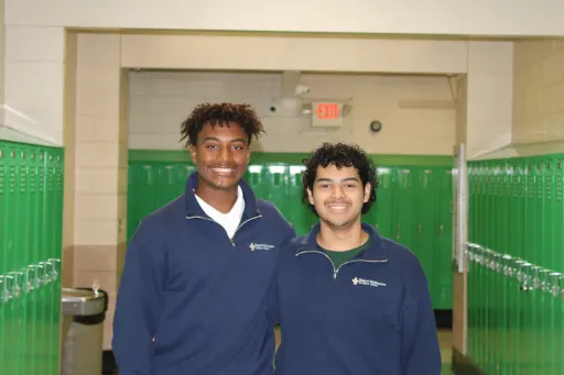 Two students standing in a hallway lined with green lockers