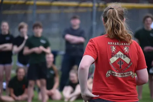 An individual with long hair tied back wears a red t-shirt with graphics on the back