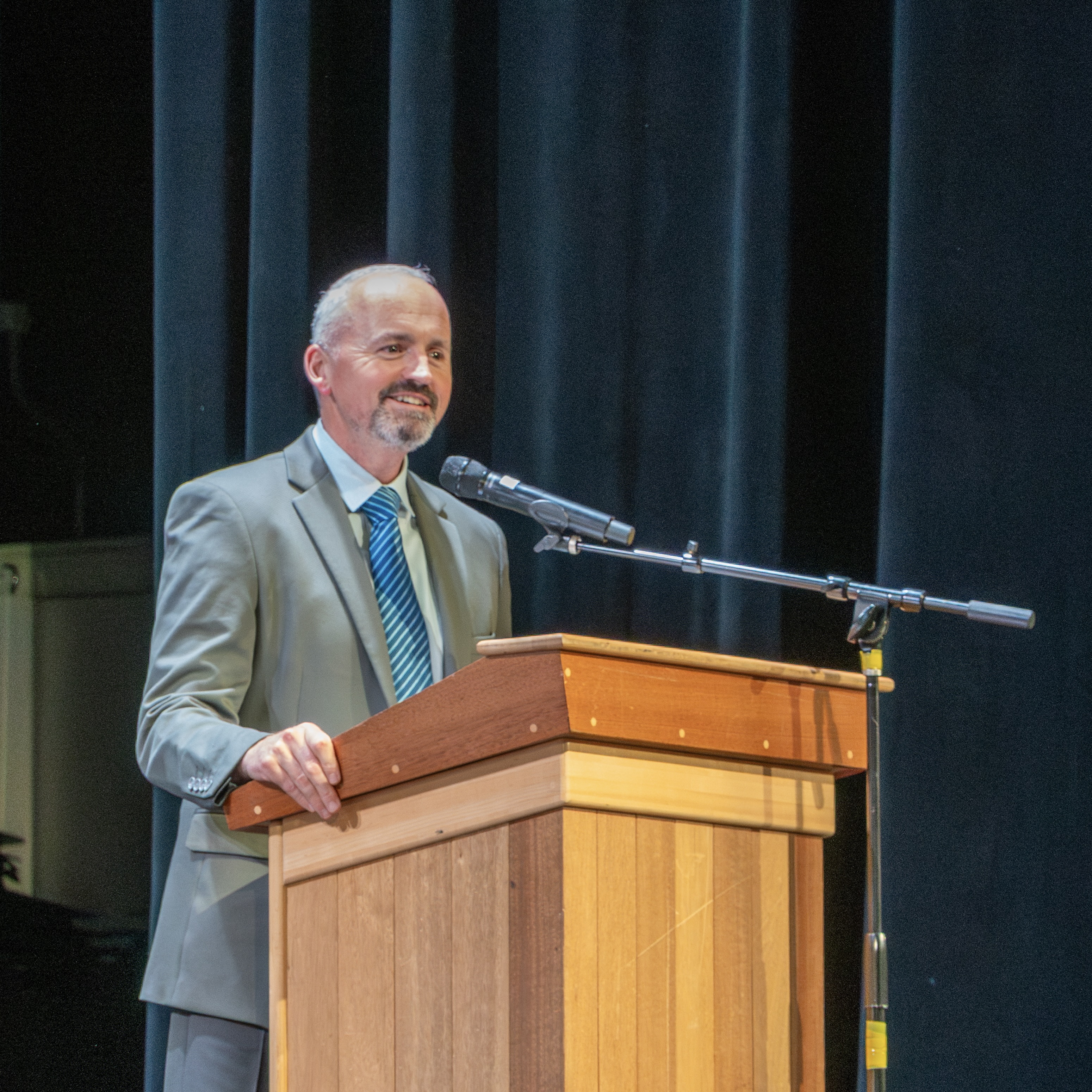 Interim Superintendent Jason DeFalco stands smiling behind a podium on stage.