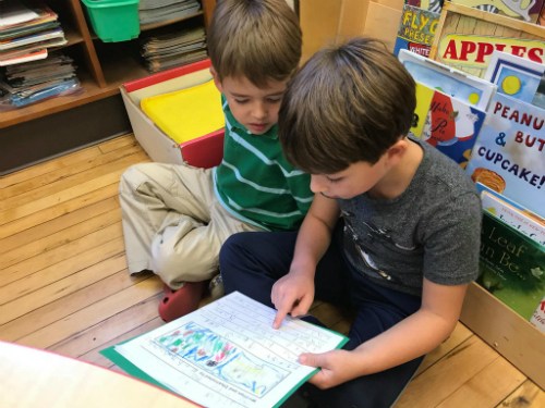 Two boys engrossed in reading a book together in a classroom setting.