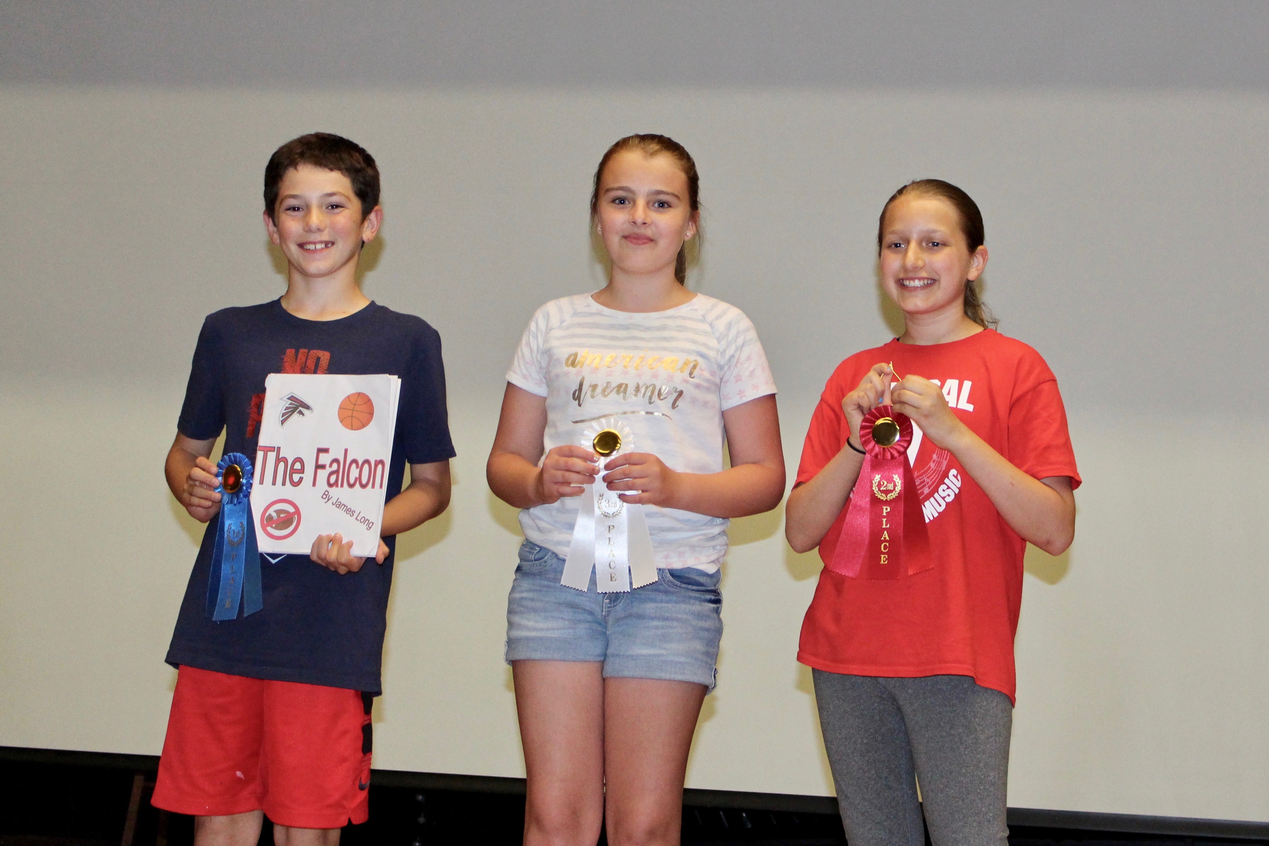 Three children proudly displaying their awards on a stage, celebrating their achievements.