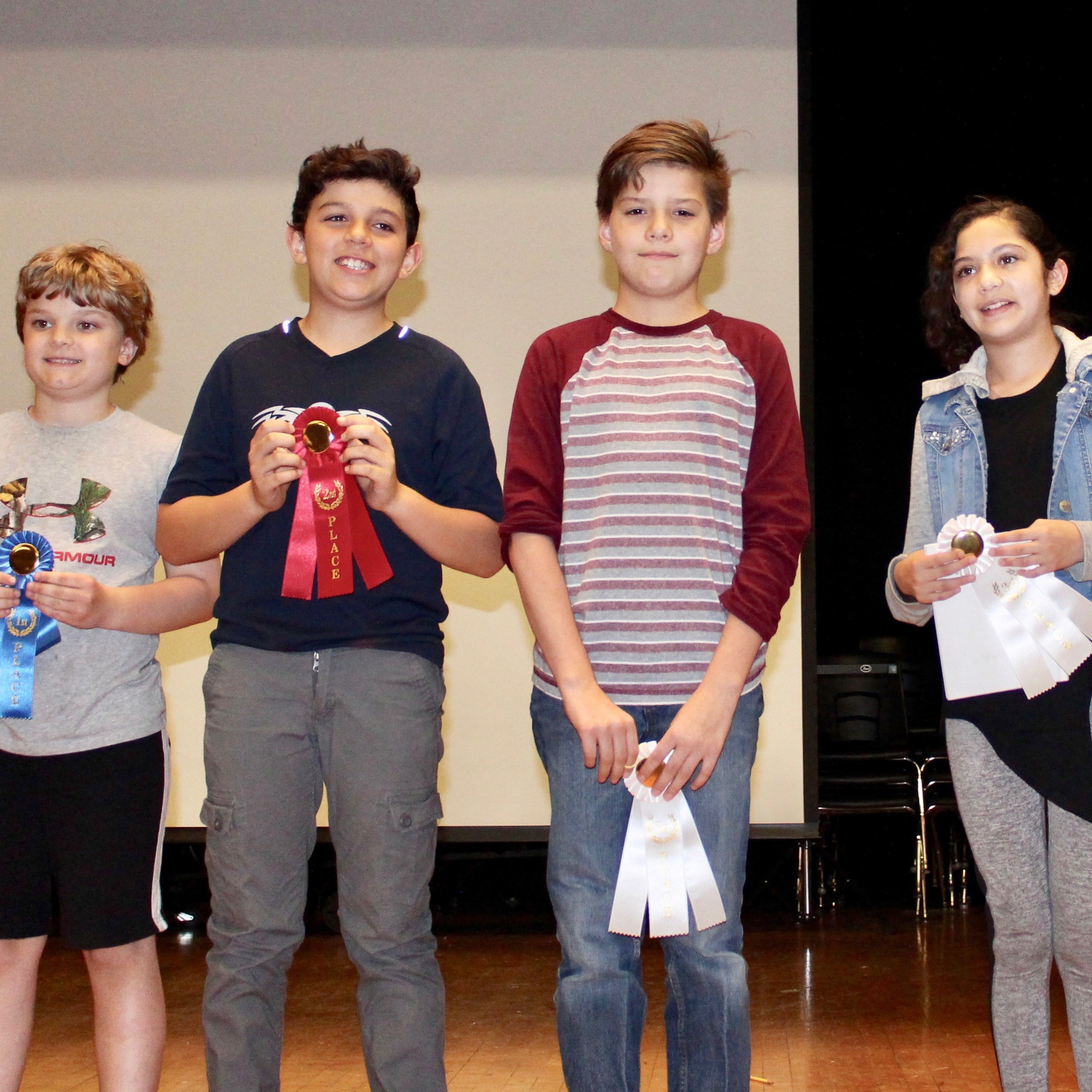 Four children on stage, holding ribbons.