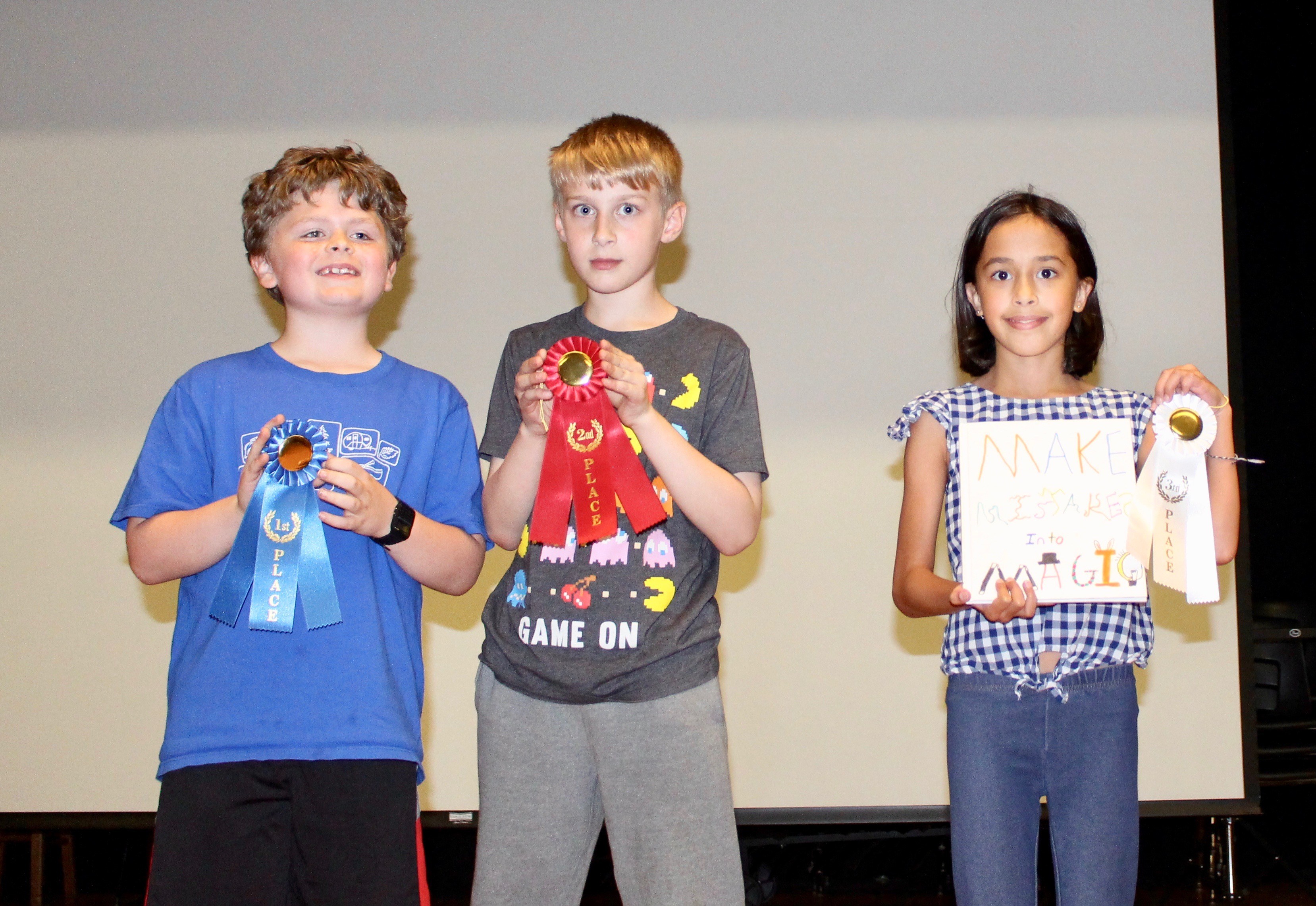 Image of three young students showcasing their achievements on stage.