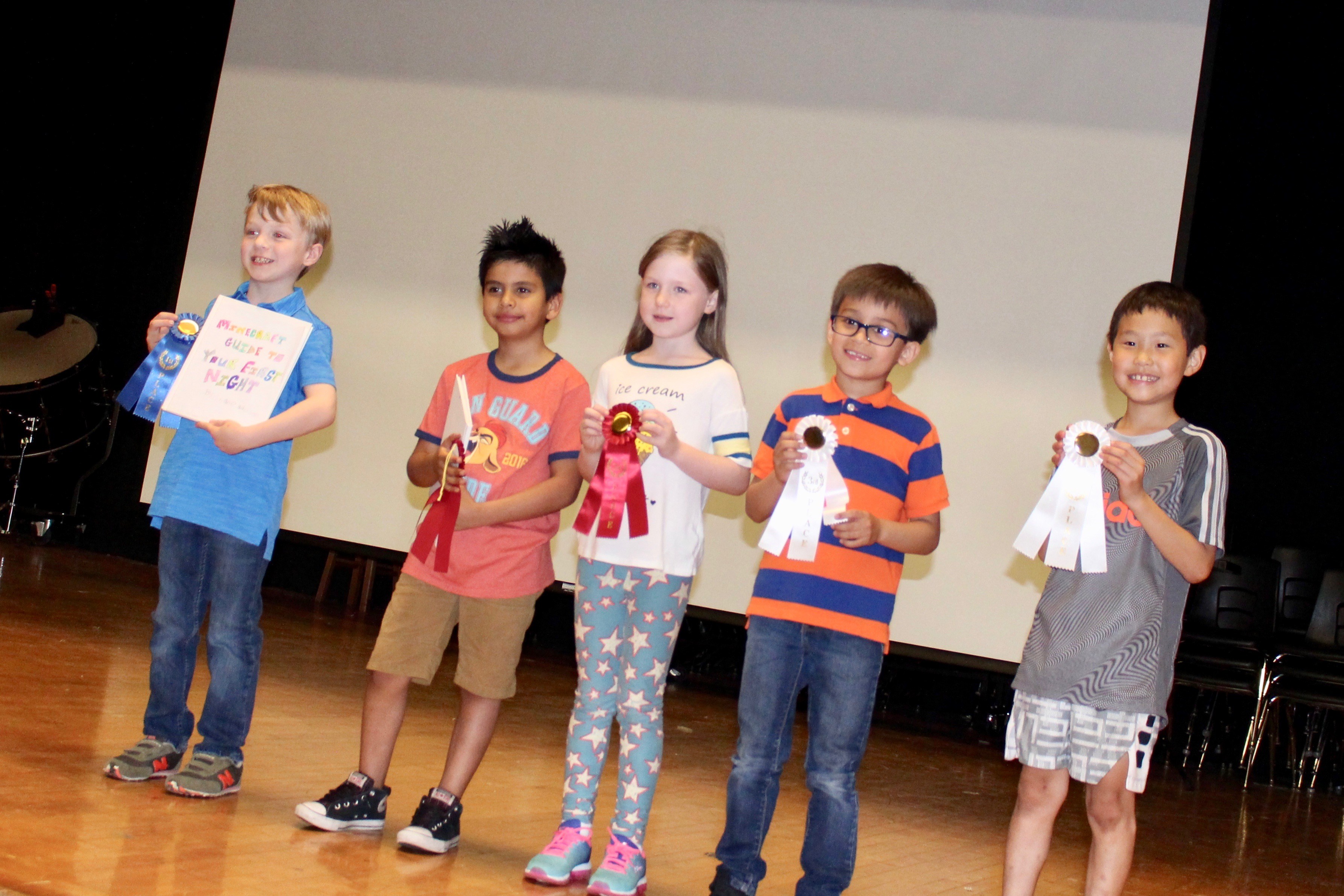 Group of kids holding up their trophies on a stage.