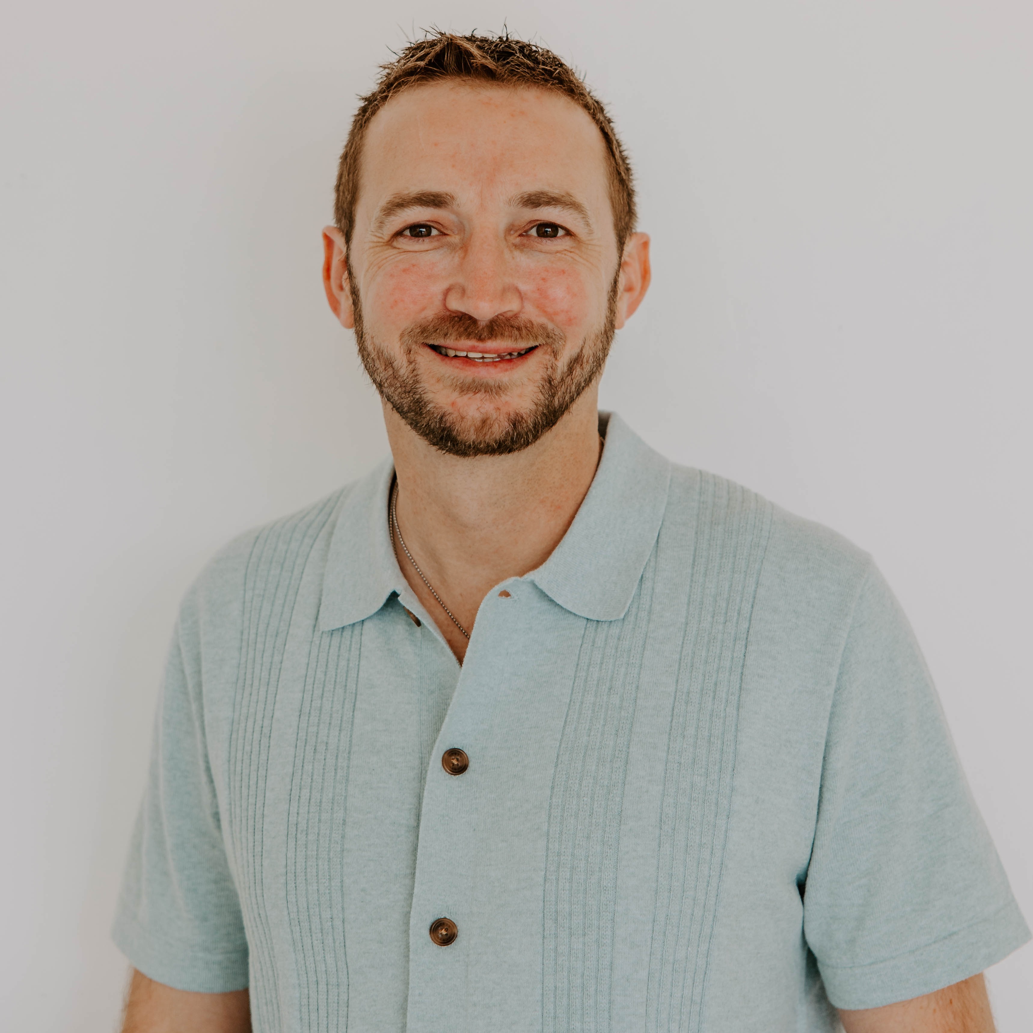 A man with glasses and a blue sweater  polo smiling.