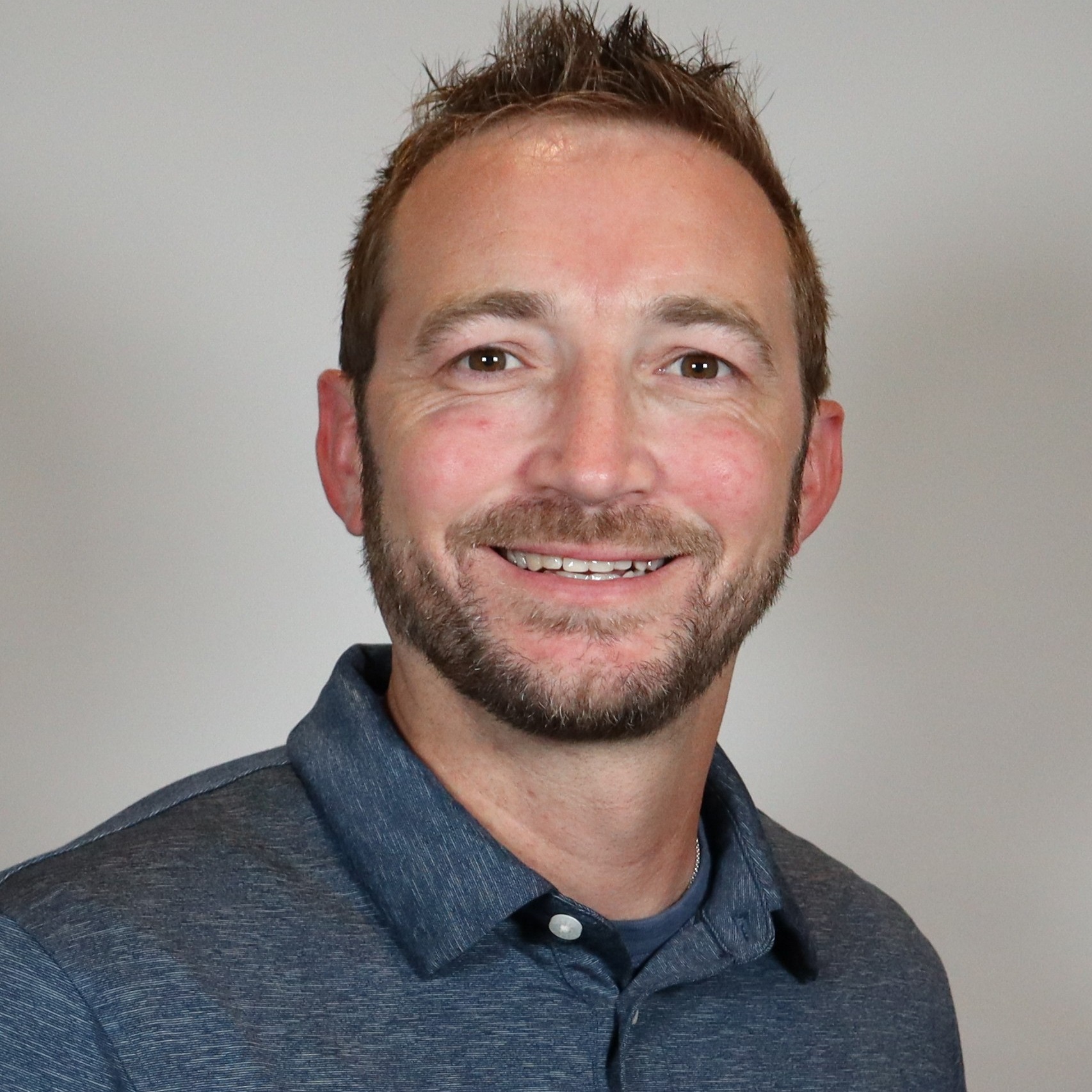 A man with glasses and a blue sweater polo smiling.