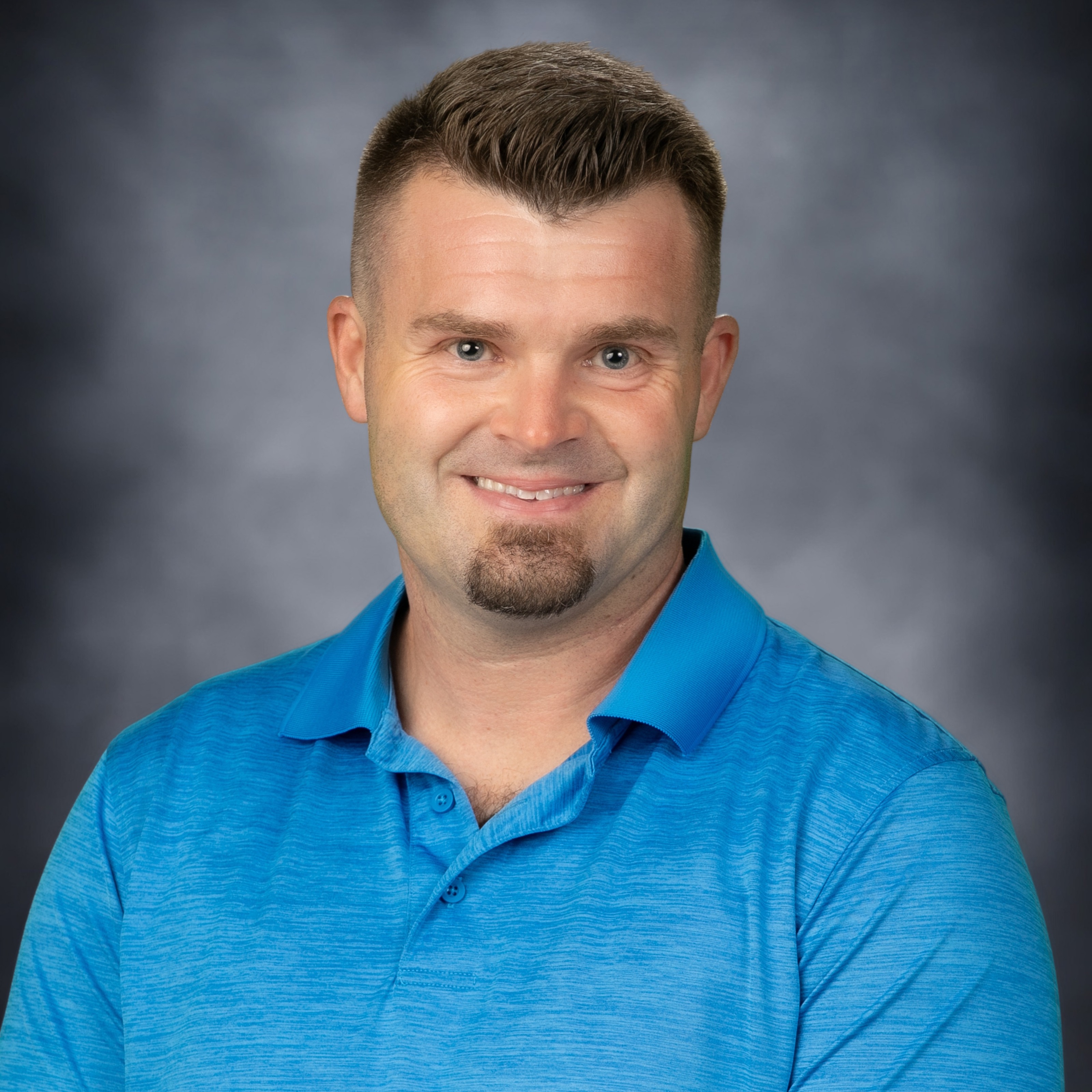 Man with a goatee and blue polo smiling