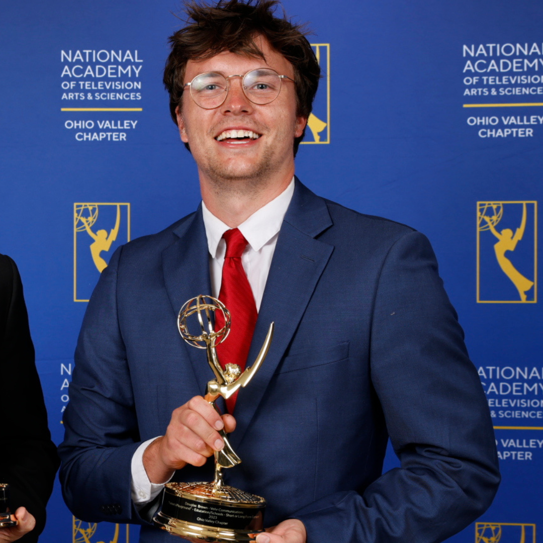 A man with scruffy hair and glasses holding an emmy in a blue suit