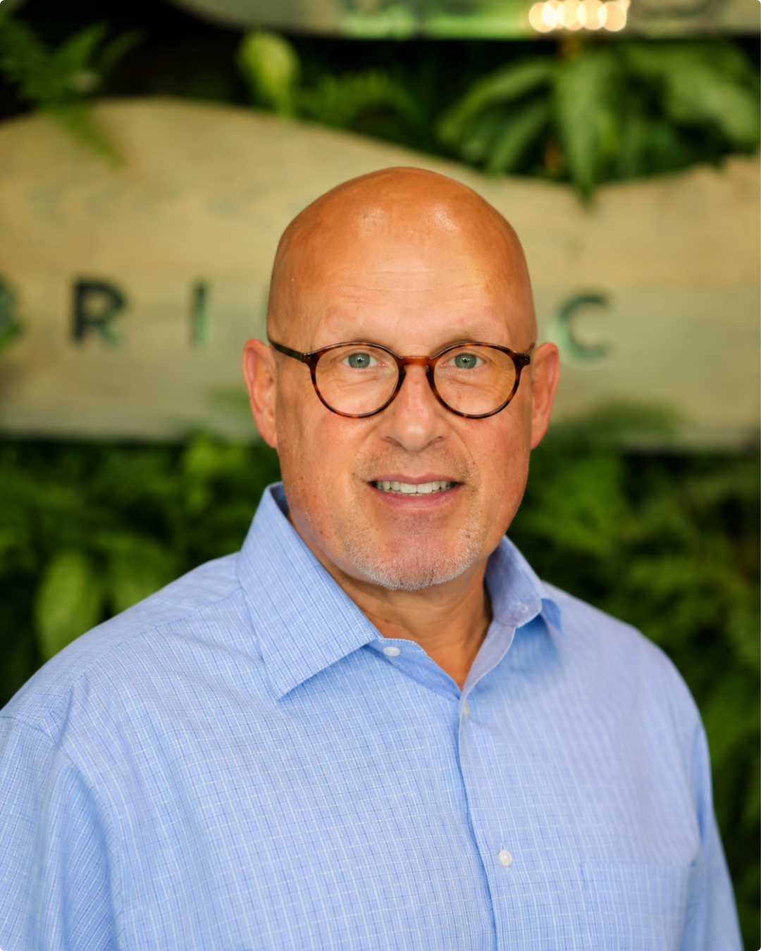 A bald man with circular red glasses in a blue checkered button up shirt