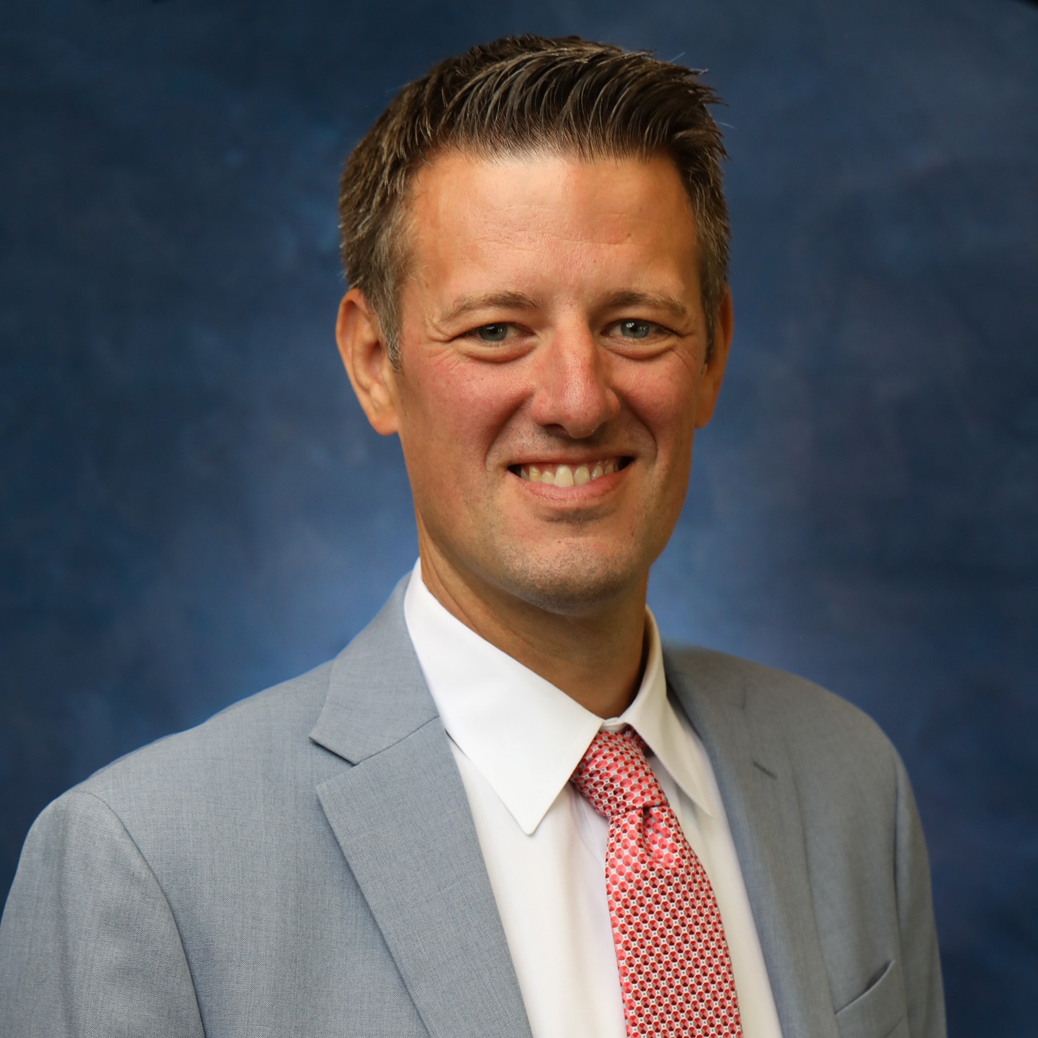 A man in a blue suit with a mint-green tie smiling at the camera