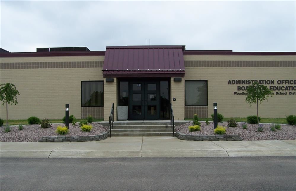 Front entrance to the administrative office building with glass doors, a sign above the entrance, and a pathway leading up to the door.