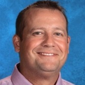 A professional man wearing a blue shirt and tie, with a pleasant smile on his face.