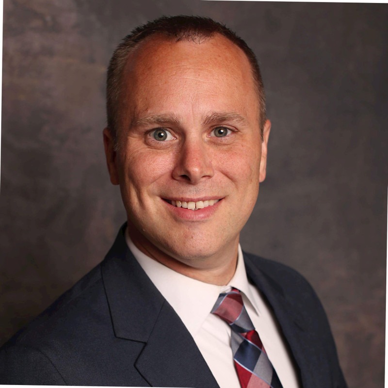 A professional man wearing a suit and tie with a pleasant expression on his face.