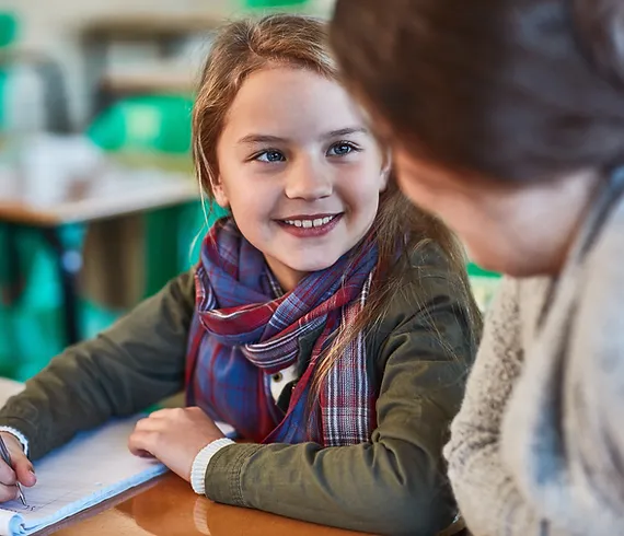 Student writing on  a paper tablet looking at their Teacher