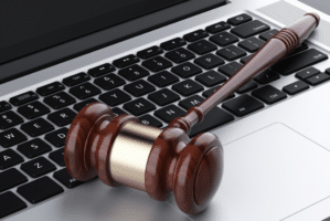 A wooden judge’s gavel resting on a laptop keyboard,